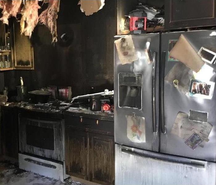 Kitchen damaged by fire, stove burned, doors of a refrigerator covered with smoke from fire, ceiling collapsed from kitchen